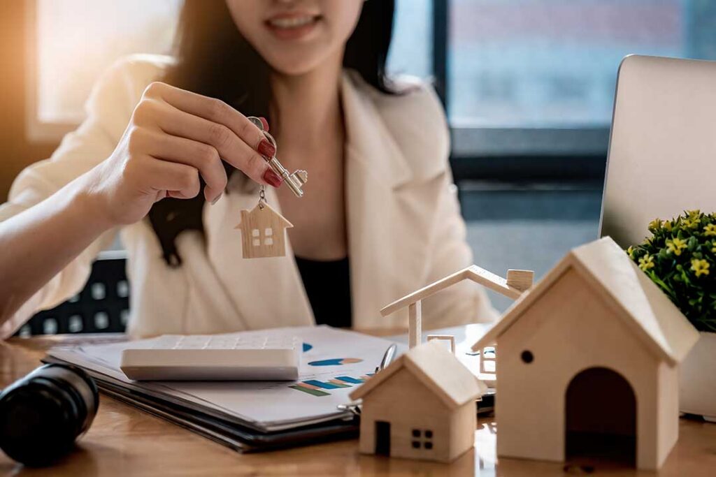 A person reviewing a paper real estate listing with a pen and highlighted notes at a wooden kitchen table.
